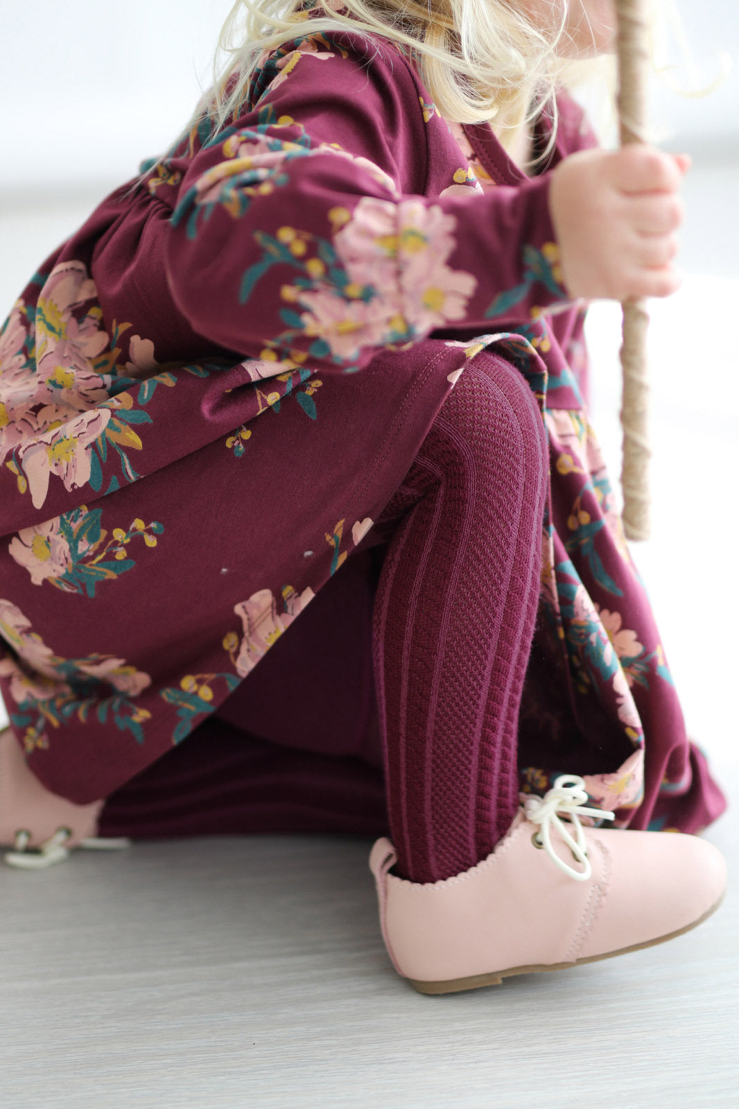 Girl in Burgundy Long Sleeve Dress, Wanders Shoe and Knitted Footed Tights in Burgundy, all designed by Burrow and Be