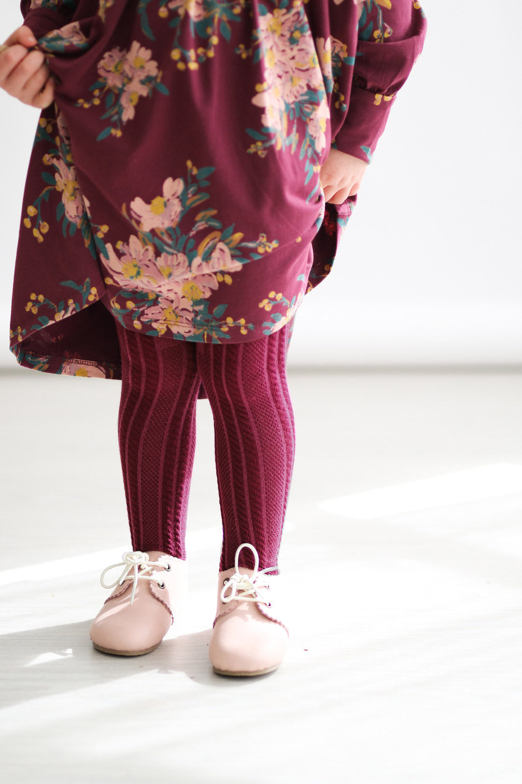 Girl posing in Burgundy Long Sleeve Dress, Wanders Shoe and Knitted Footed Tights in Burgundy, all designed by Burrow and Be