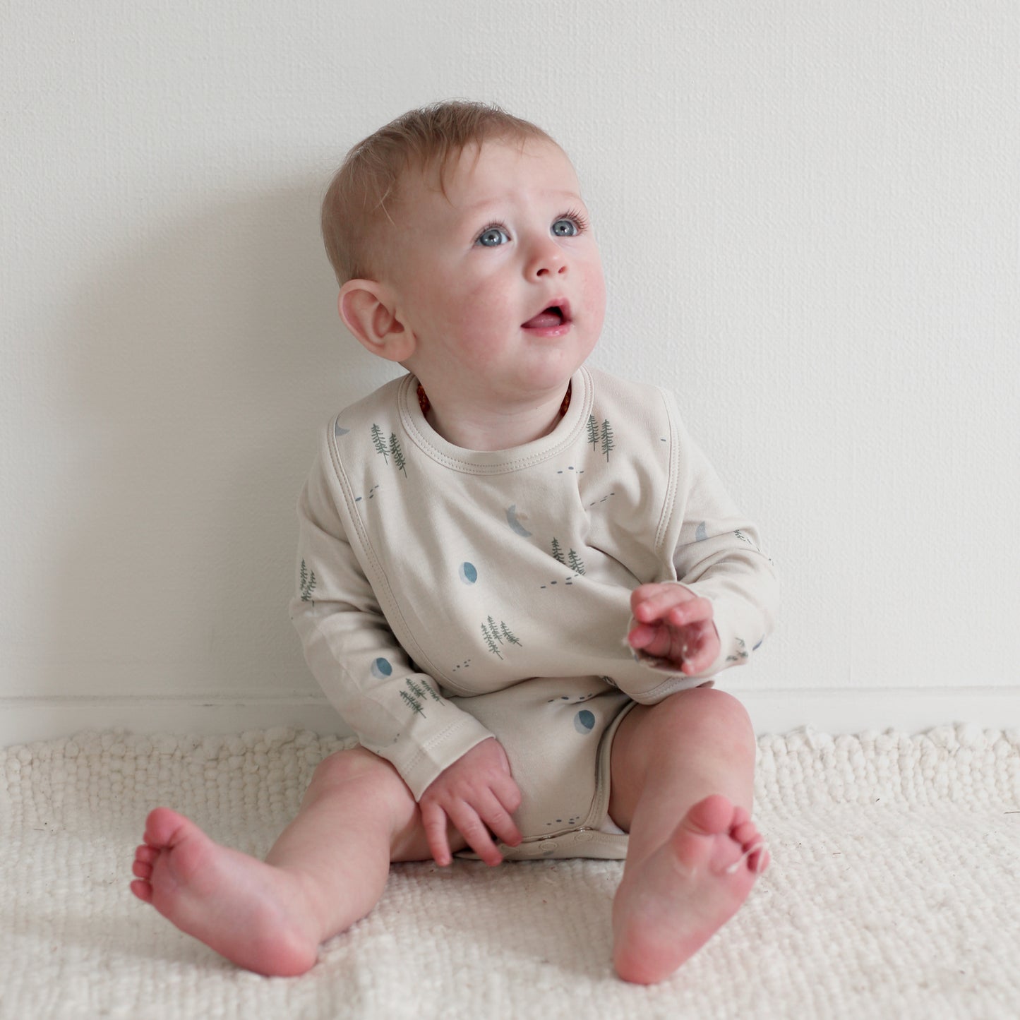 Toddler sitting on floor wearing Burrow and Be Midnight Forest Snuggle Bib