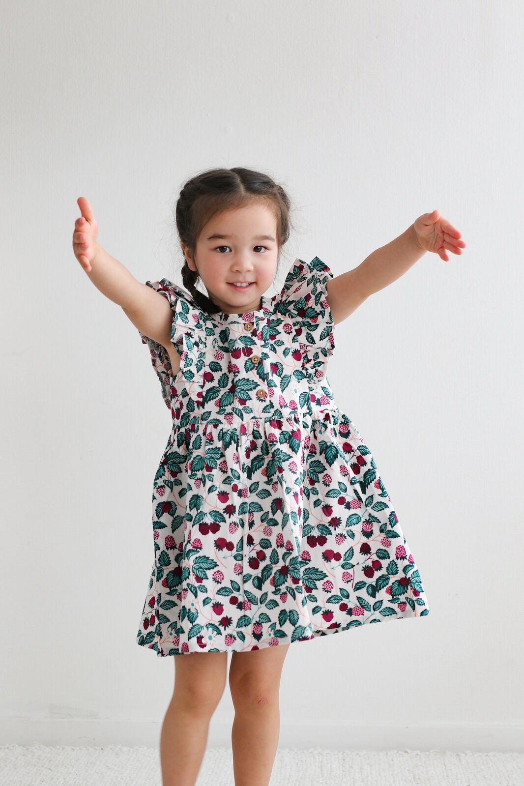 Child wearing a floral dress with arms raised on a plain background