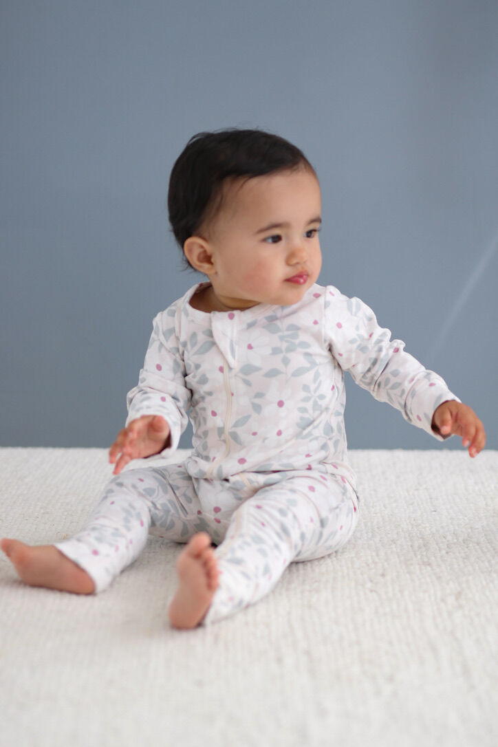 Baby sitting on a white surface wearing a patterned onesie against a gray background