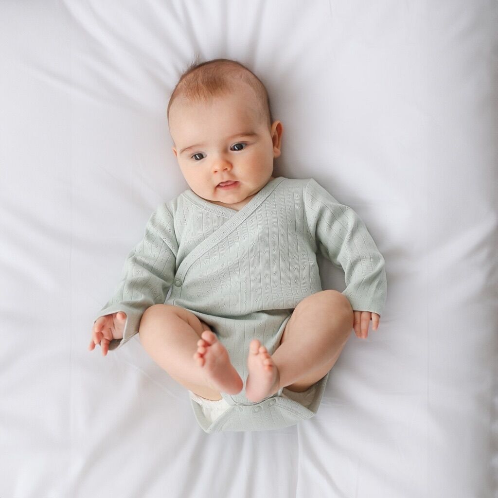 Baby wearing a light green onesie lying on a white surface