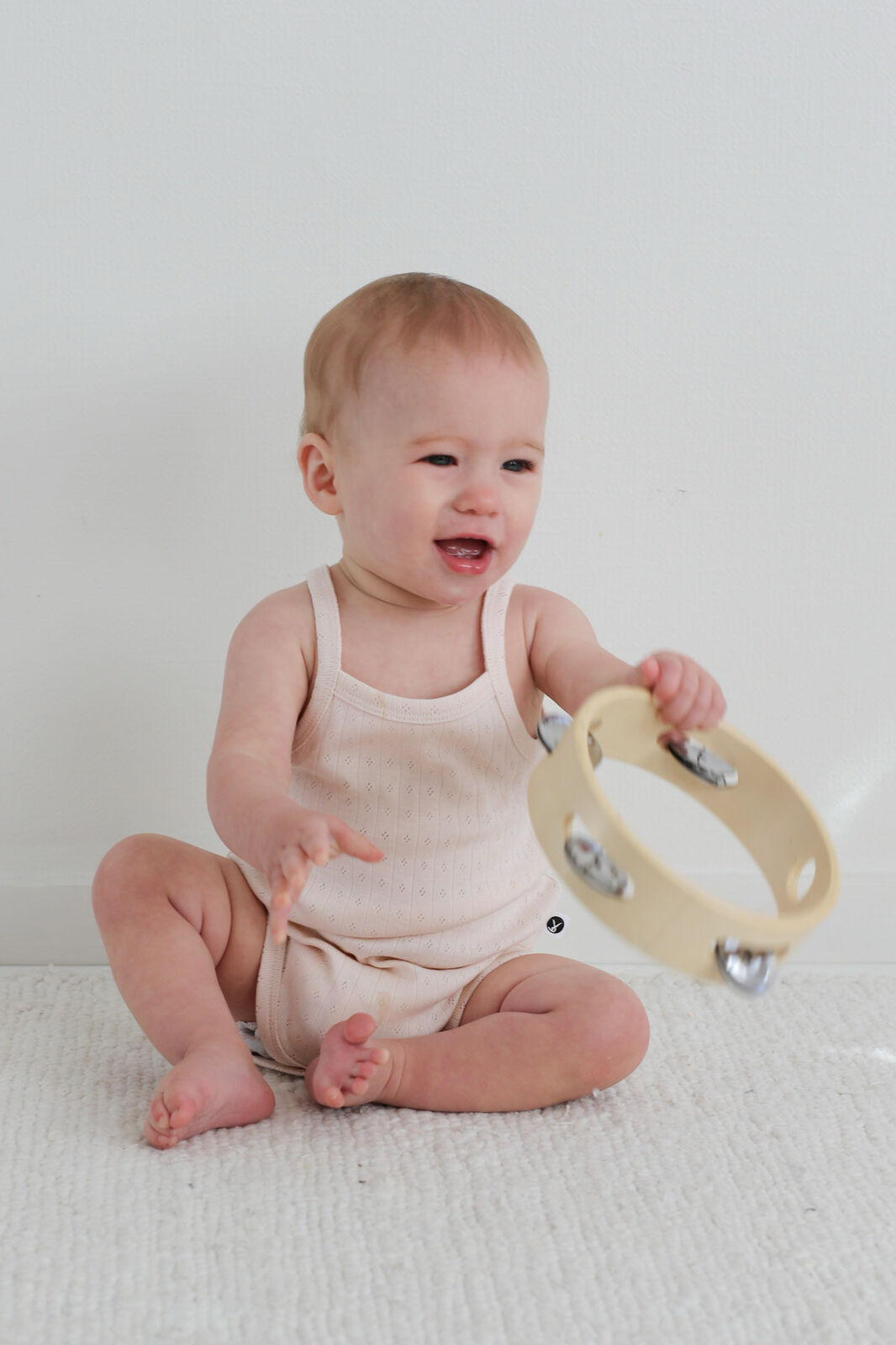 Baby sitting on a white surface holding a wooden tambourine.