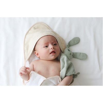 Baby hugging bunny doll and wrapped in Dusty Rose Essential Baby Hooded Towel designed by Burrow and Be
