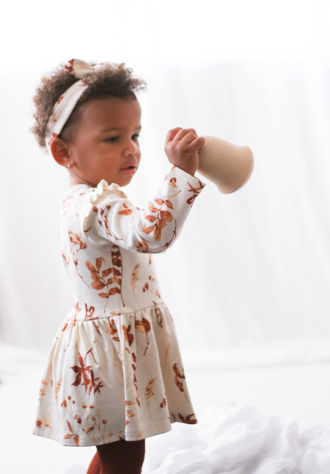 Baby girl wearing Flutter Dress and Essential Baby Headband both in Autumn Leaves print, designed by Burrow and Be