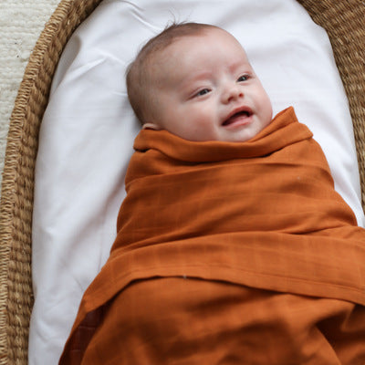Baby in a Moses Basket wrapped in Essential Muslin Wrap in Rust, designed by Burrow and Be