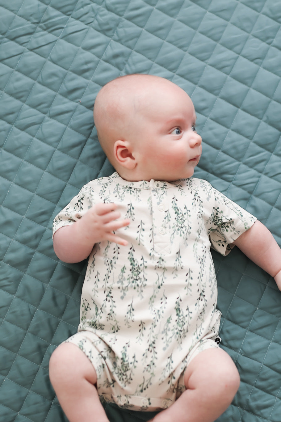 Baby wearing String of Pearls Alex Romper from Burrow and Be and lying on quilted sage mat
