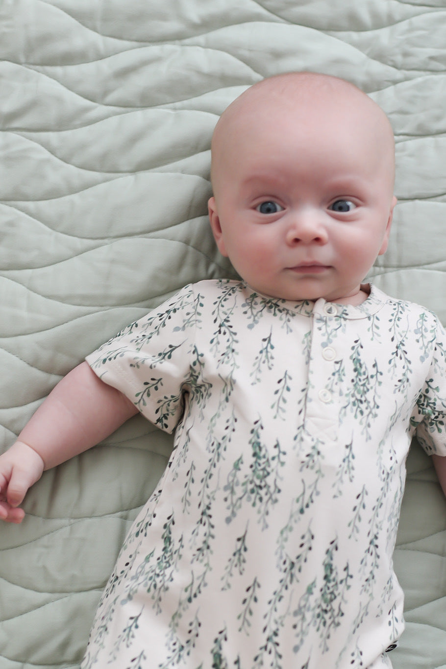 Infant lying on Mist Quilted Mat and wearing String of Pearls Alex Romper, both from Burrow and Be