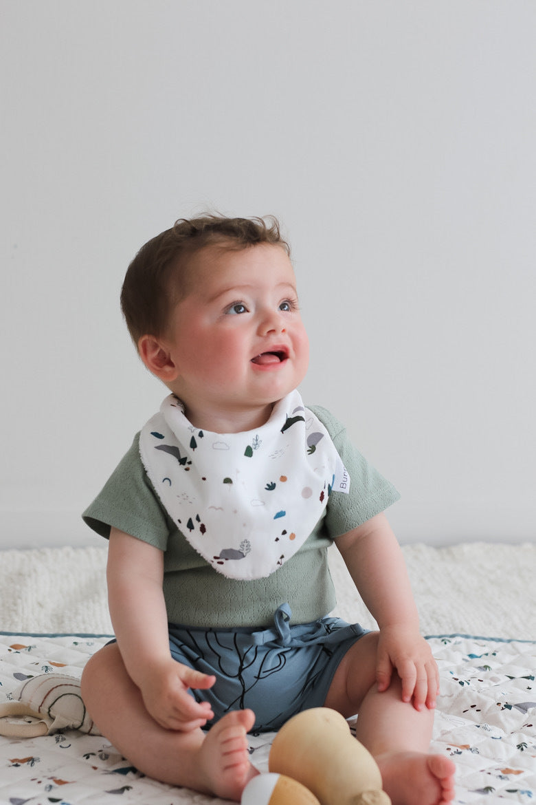 Baby wearing Sage Pointelle Bodysuit and Giant Bugs shorts with Garden Treasure Baby Dribble Bib, all designed by Burrow and Be