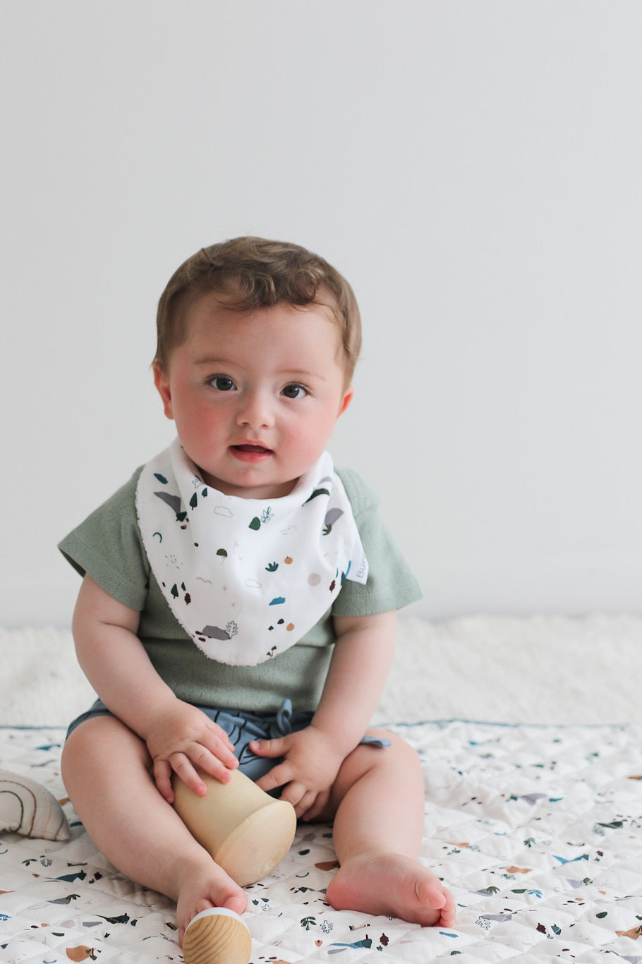 Baby sitting on Garden Treasure Quilted Mat and wearing Sage Pointelle Bodysuit and Giant Bugs shorts with Garden Treasure Baby Dribble Bib, all designed by Burrow and Be