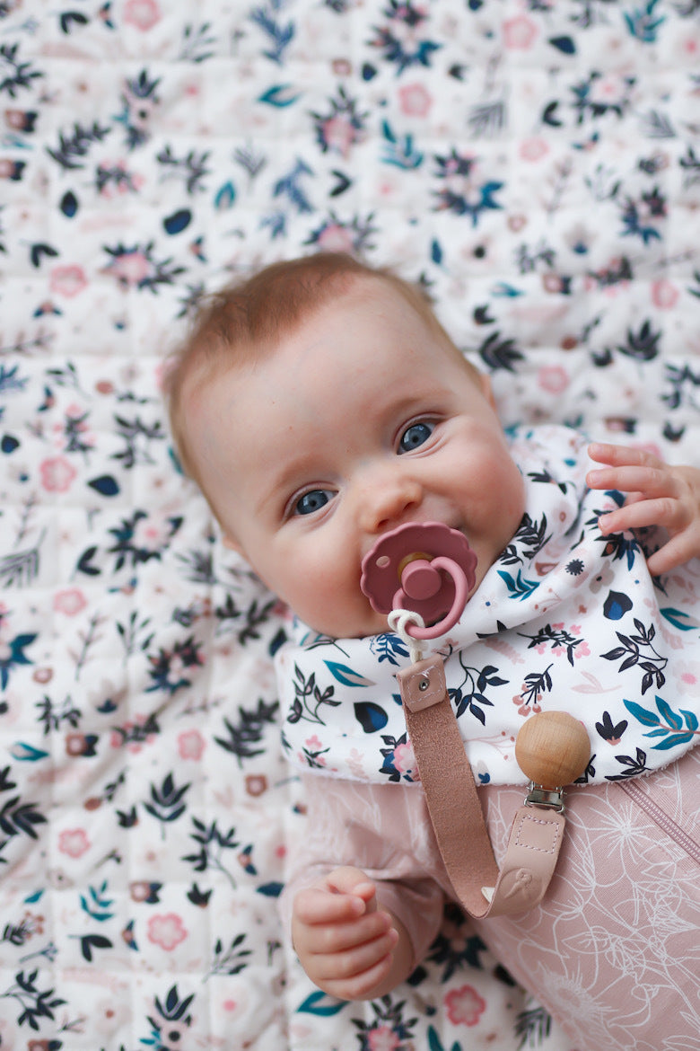 Baby wearing Botanica Zip Suit with Petite Clementine Baby Dribble Bib, all designed by Burrow and Be and lying down on Petite Clementine Quilted Mat