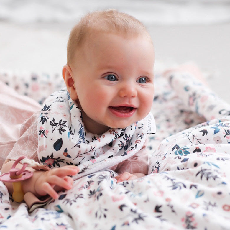 Baby lying down on soft Petite Clementine bedsheets while wearing Botanica Zip Suit with Petite Clementine Baby Dribble Bib and pacifier clip, all designed by Burrow and Be