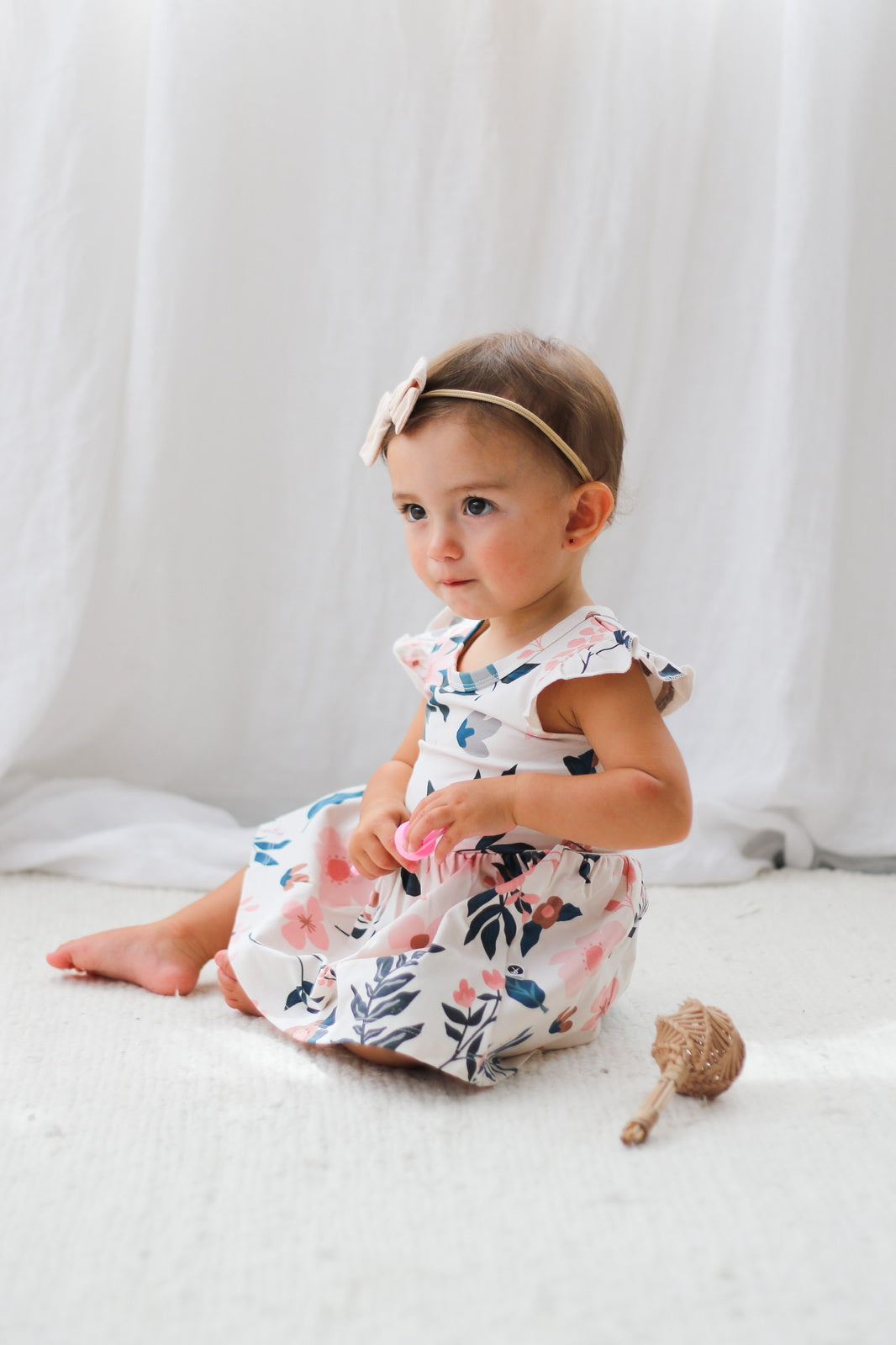 Baby sitting on carpet and wearing Bow Tie Hair Tie and Pink Clementine Flutter Baby Dress, all designed by Burrow and Be