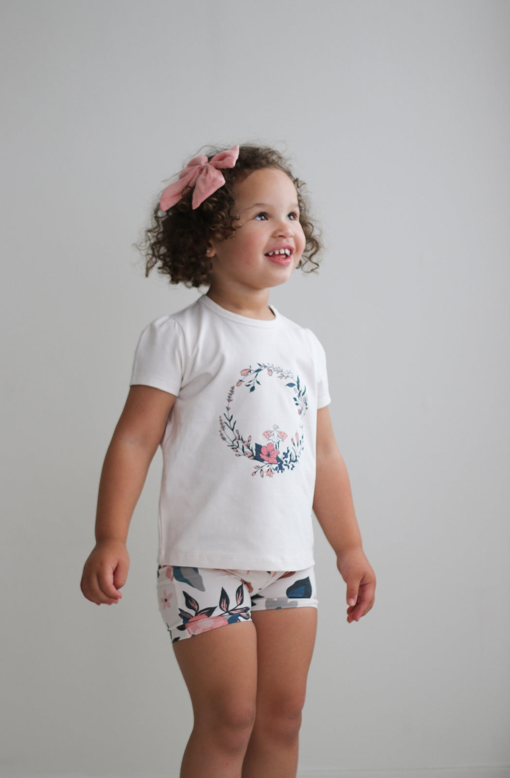 Girl posing against a white background and wearing Fairy Wreath T-shirt and Pink Clementine Bike Shorts, both designed by Burrow and be