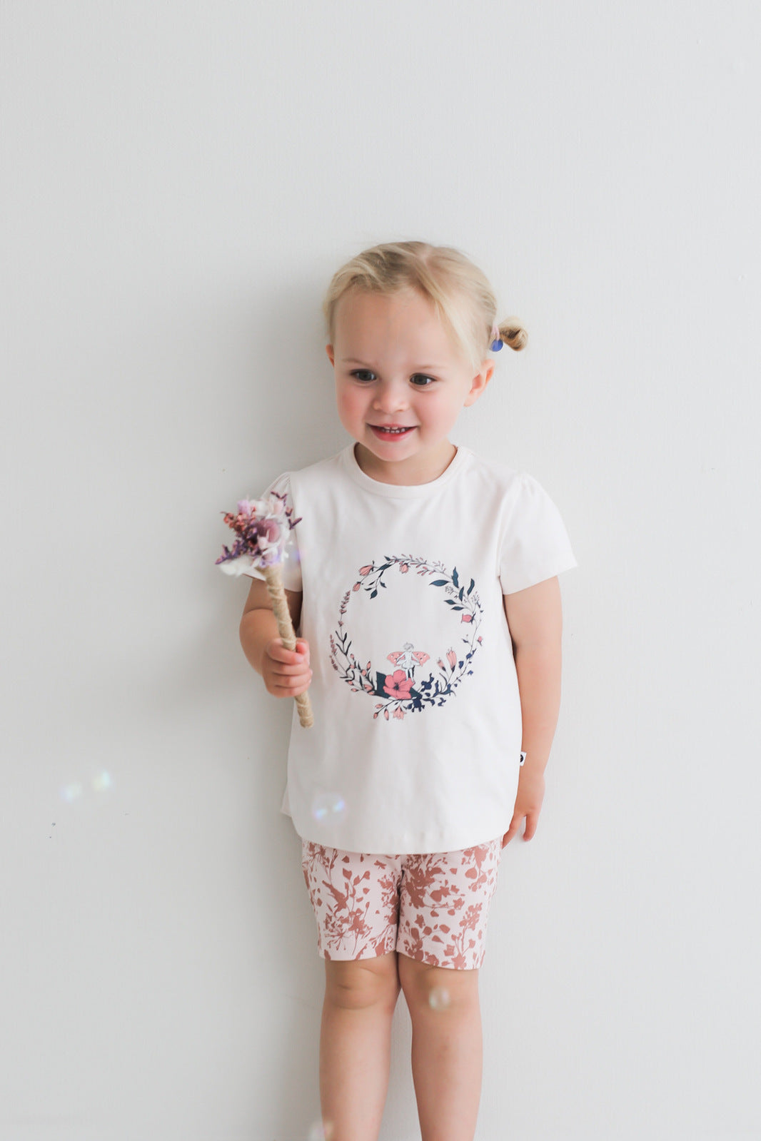 Girl standing against a white background while wearing Fairy Wreath T-shirt and Flower Splash Bike Shorts, all designed by Burrow and be