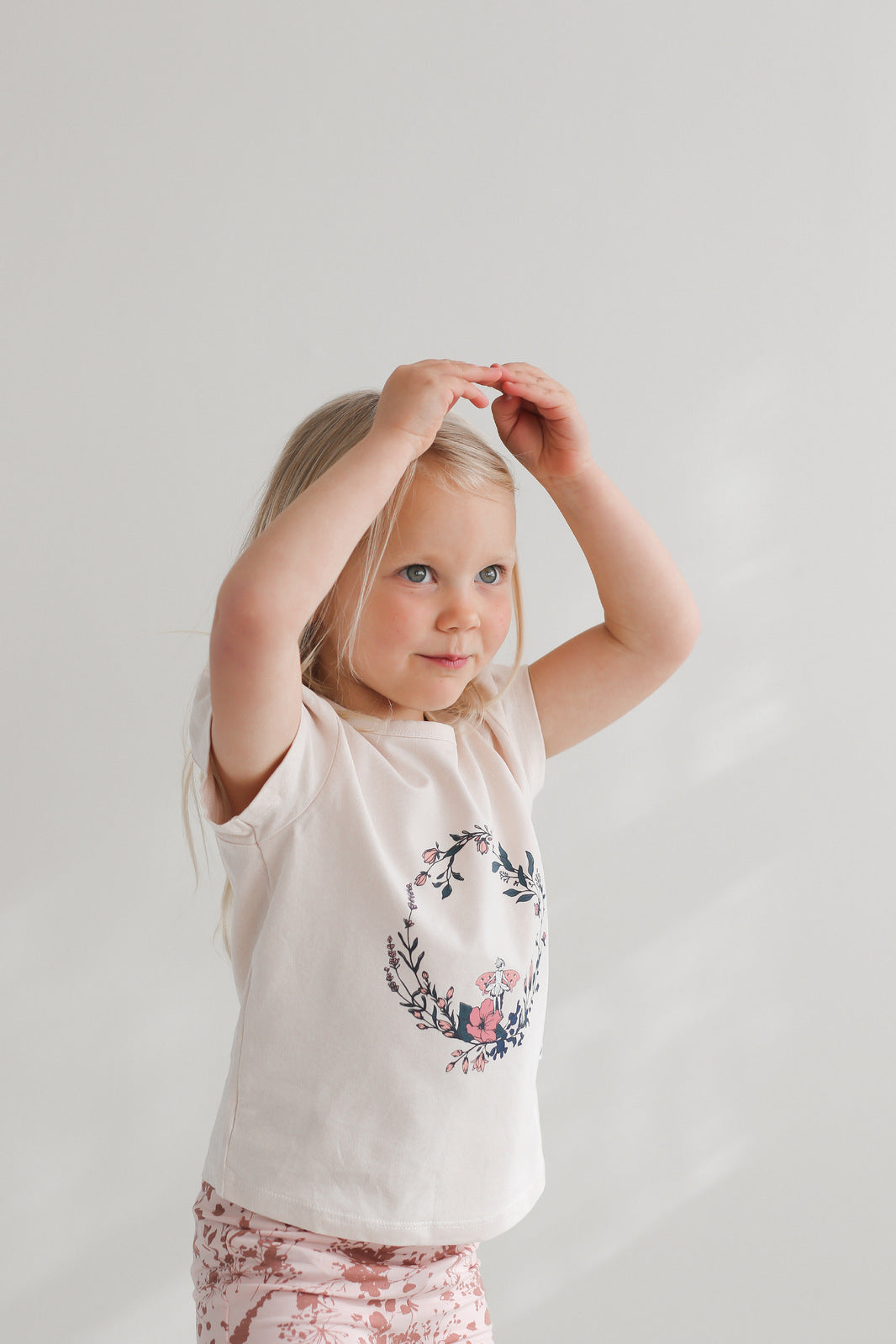 Blonde girl posing in front camera while wearing Fairy Wreath T-shirt and Flower Splash Bike Shorts, all designed by Burrow and be