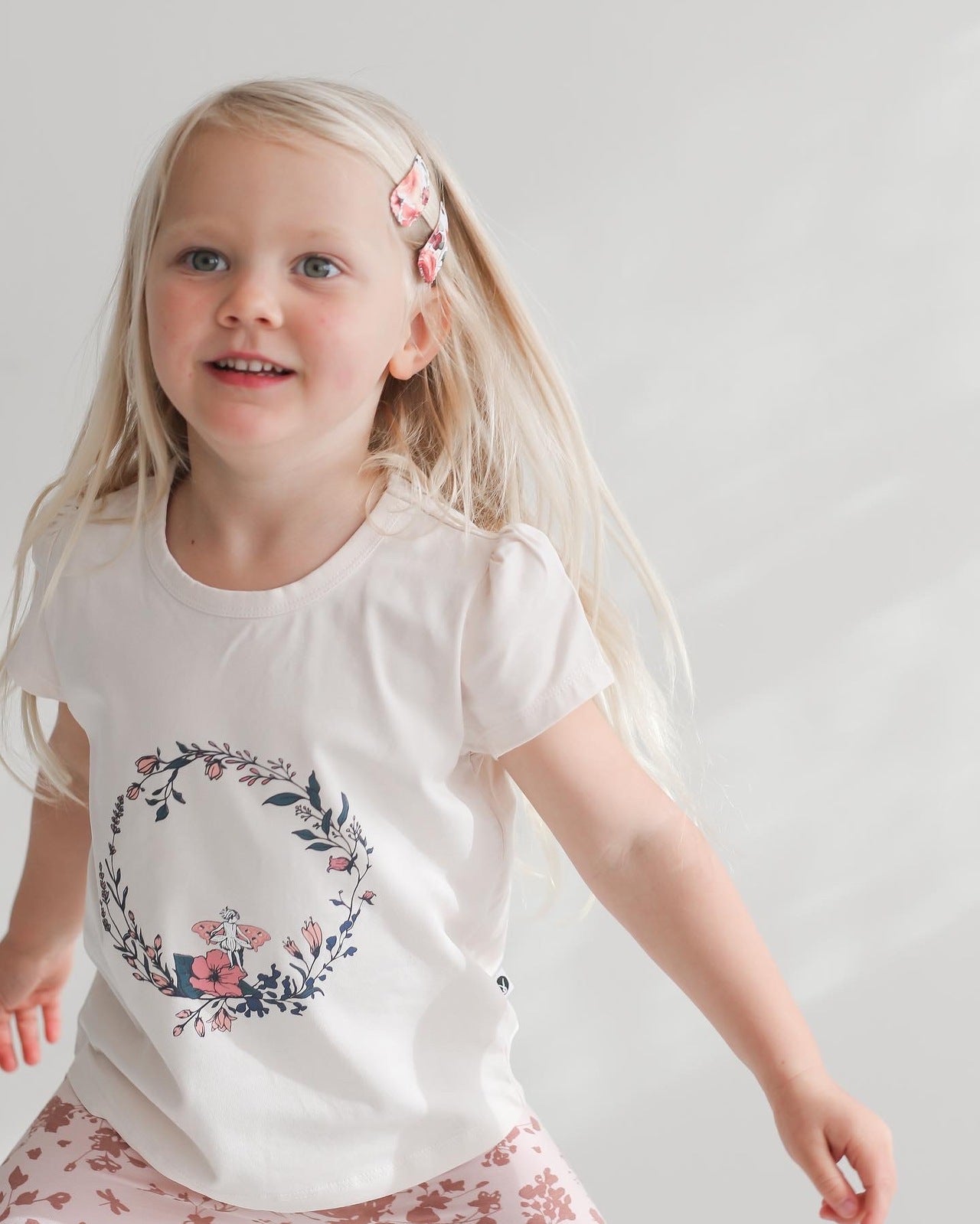 Blond girl posing in front of camera while wearing Fairy Wreath T-shirt and Flower Splash Bike Shorts, all designed by Burrow and Be