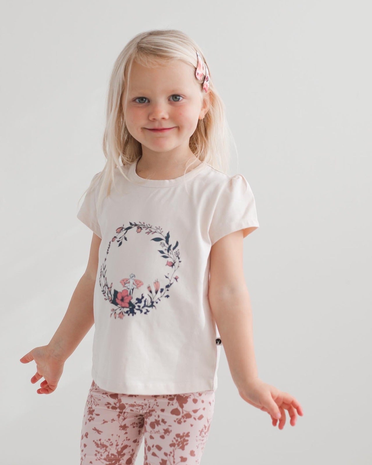 Blond girl posing in front of camera while wearing Fairy Wreath T-shirt and Flower Splash Bike Shorts, all designed by Burrow and Be