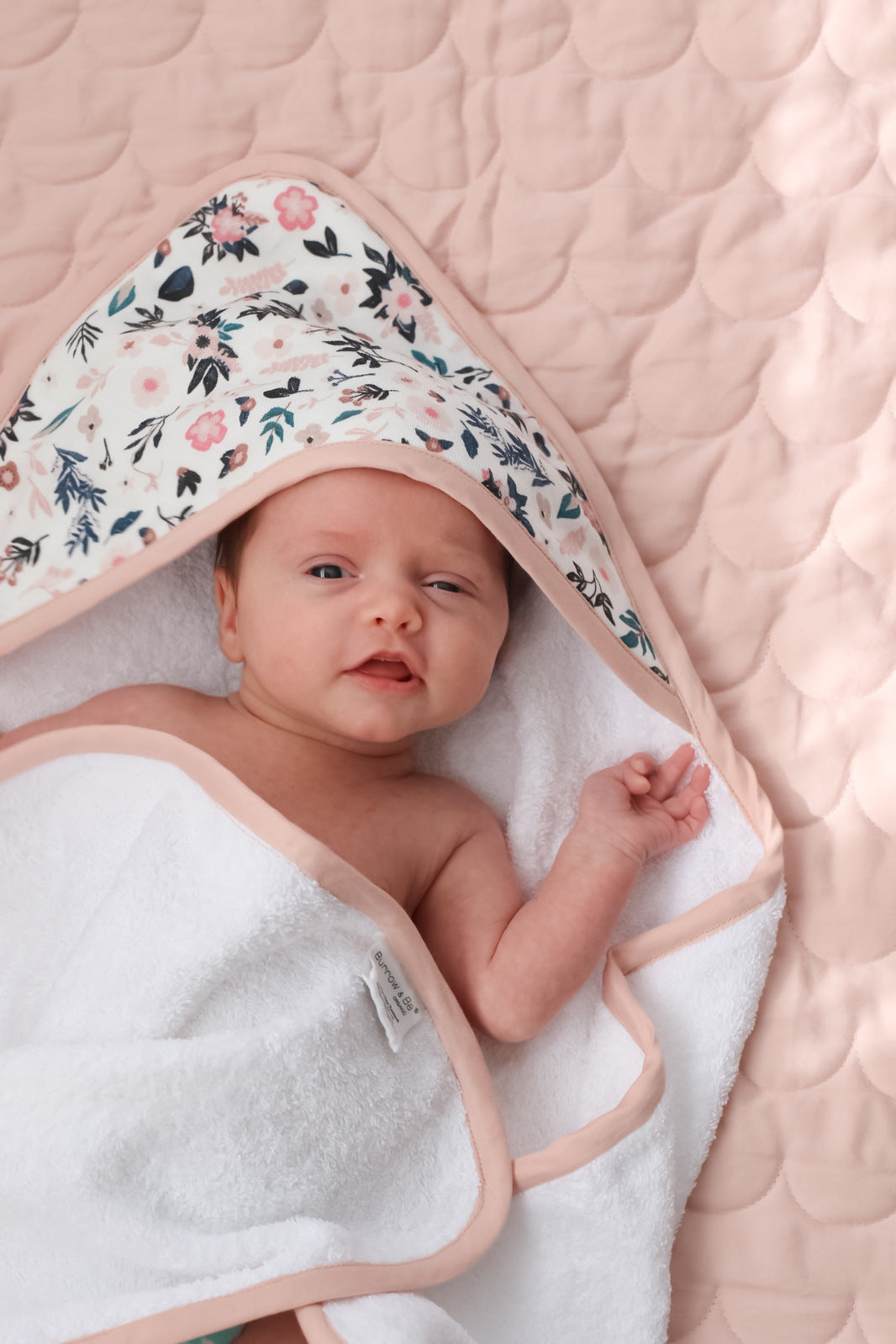 Baby laying on Quilted Mat in Blush and wrapped in Petite Clementine Baby Hooded Towel, both designed by Burrow and Be