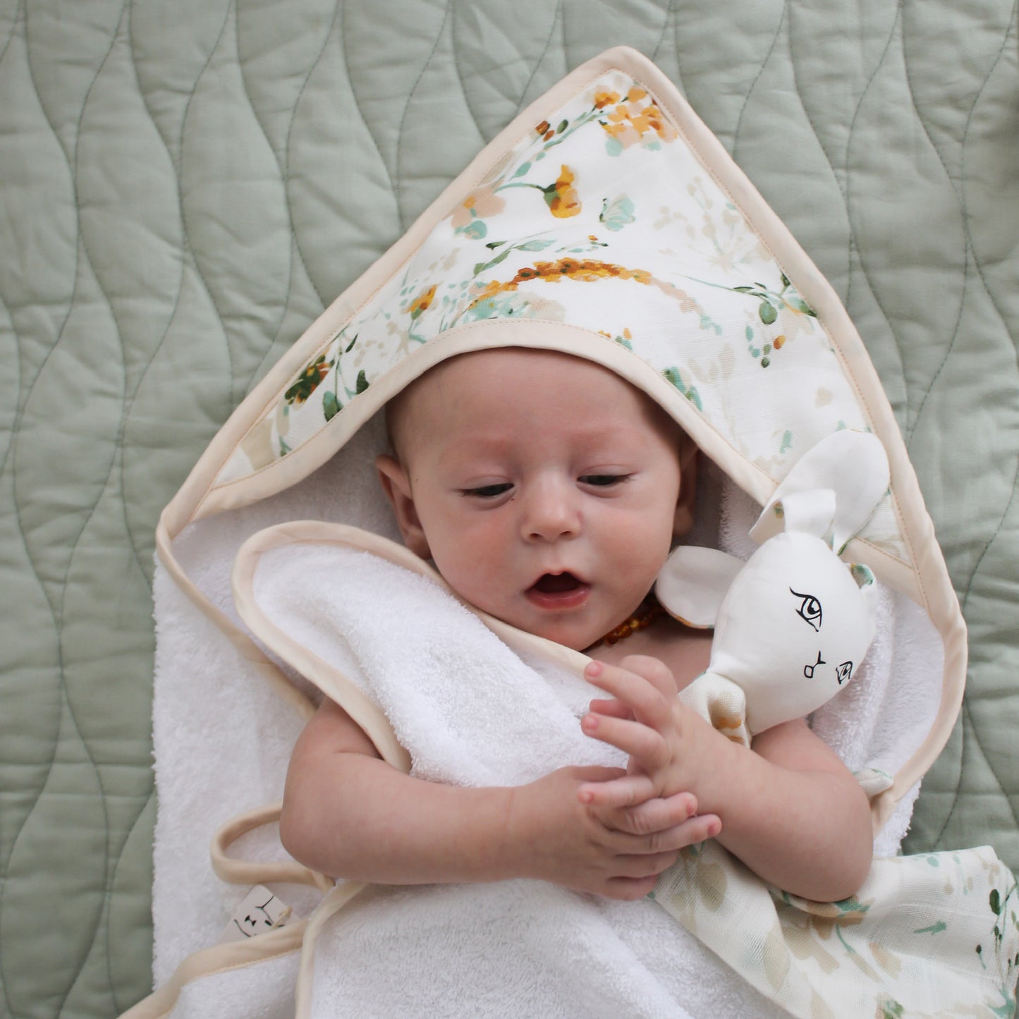 Baby laying on Essential Quilted Mat in Dusty Rose and wrapped in Spring Melody Baby Hooded Towel, both designed by Burrow and Be