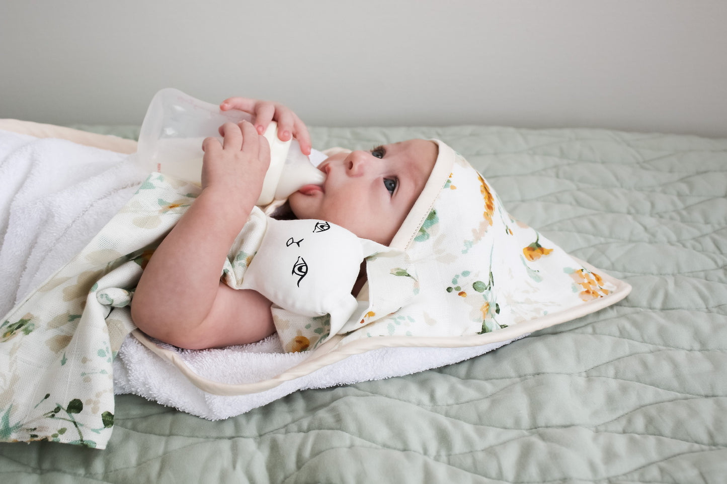 Baby laying on Essential Quilted Mat in Dusty Rose and wrapped in Spring Melody Baby Hooded Towel, both designed by Burrow and Be