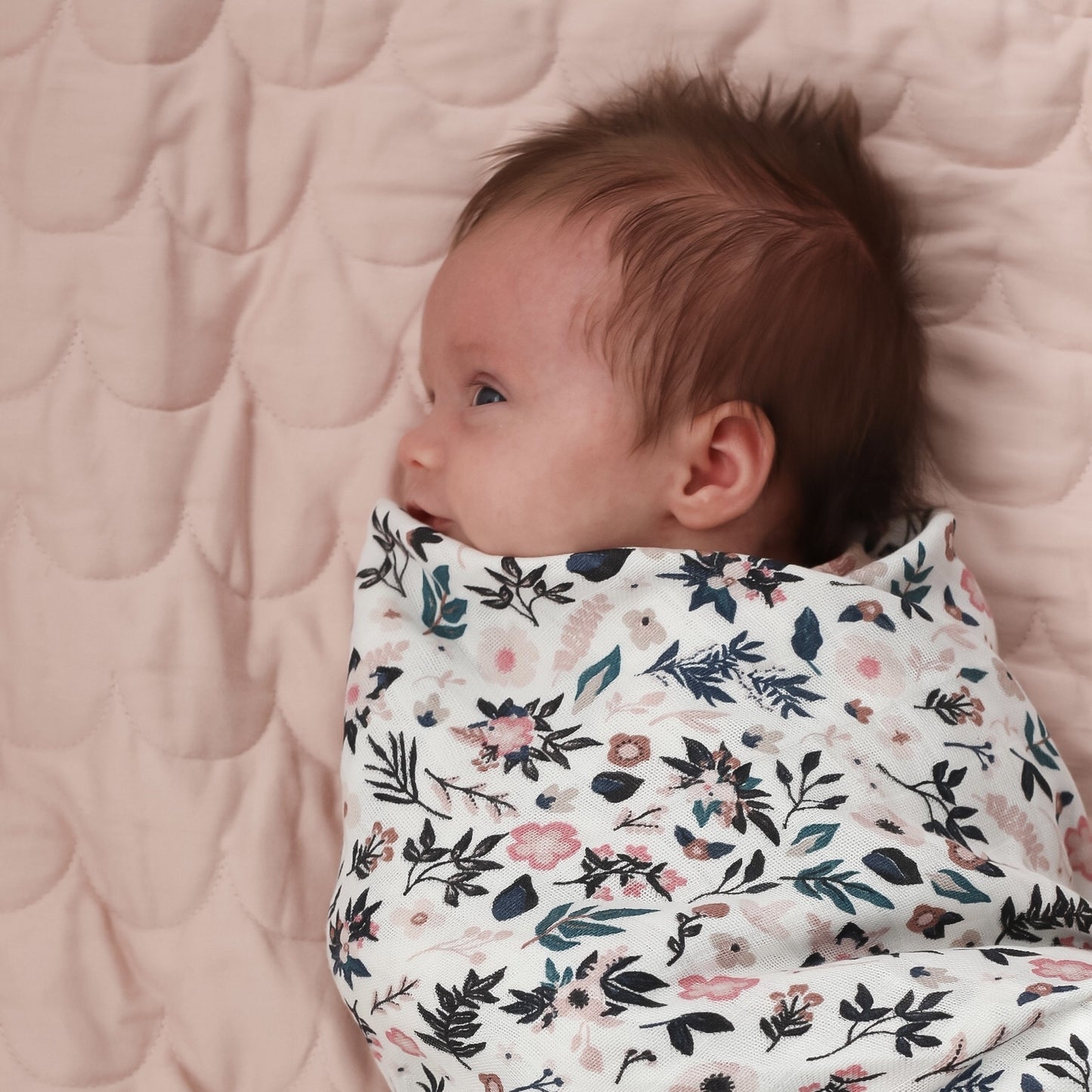 Baby laying on Quilted Mat and wrapped in Petite Clementine Muslin Wrap, designed by Burrow and Be
