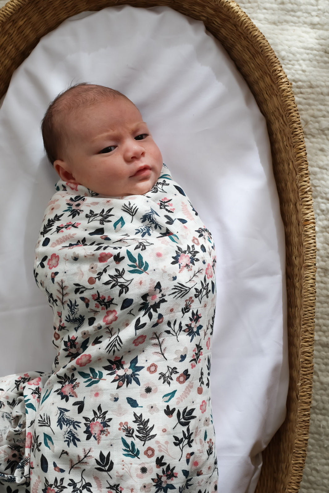 Baby laying in Moses Basket and wrapped in Petite Clementine Muslin Wrap, designed by Burrow and Be
