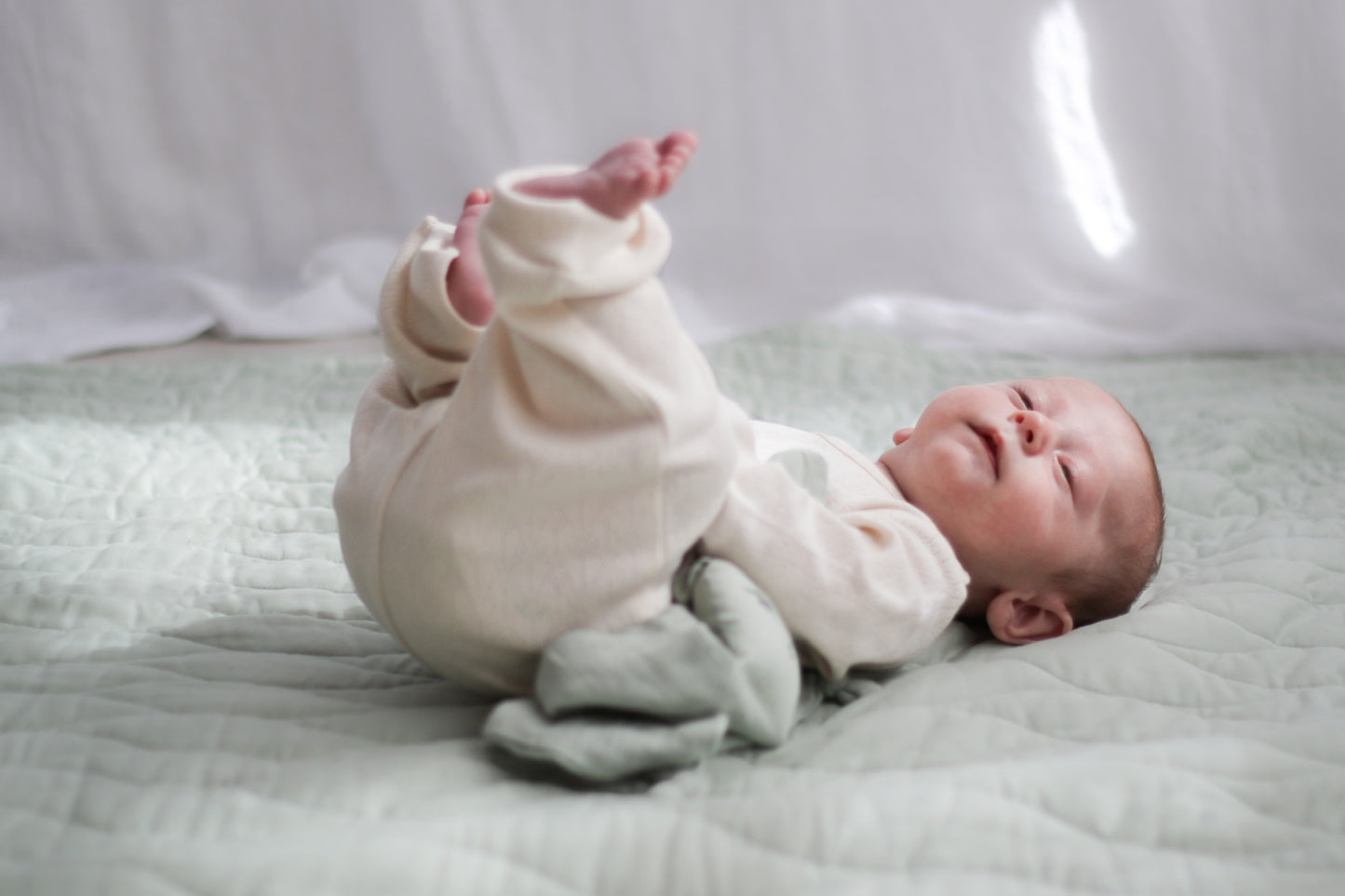Baby laying on Sage Quilted Mat while wearing Pointelle Baby Pants in Natural, both designed by Burrow and Be