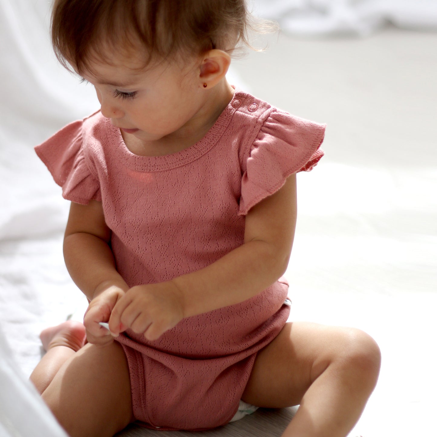 Baby sitting on carpet and wearing Pointelle Flutter Sleeve Bodysuit in Dusk, designed by Burrow and Be