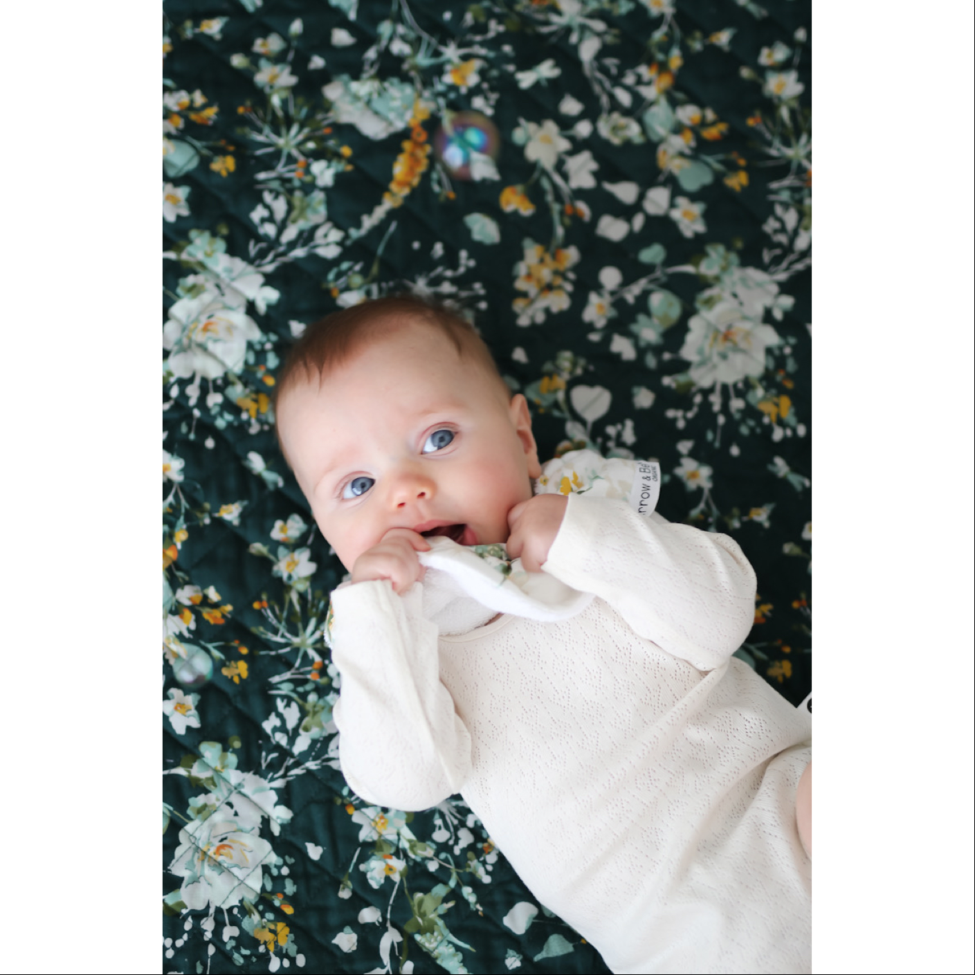 Close up of baby laying on Green Leavings Quilted Mat while wearing Leavings Dribble Bib, Pointelle Long Sleeve Bodysuit and Baby Pants in Natural, all designed by Burrow and Be