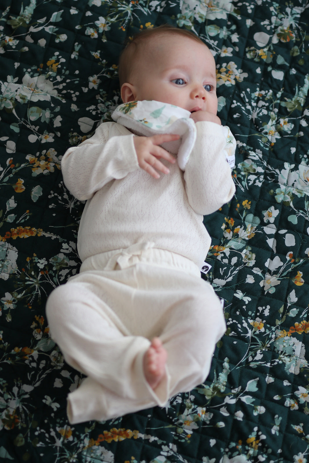 Baby laying on Green Leavings Quilted Mat while wearing Pointelle Long Sleeve Bodysuit and Baby Pants in Natural, all designed by Burrow and Be