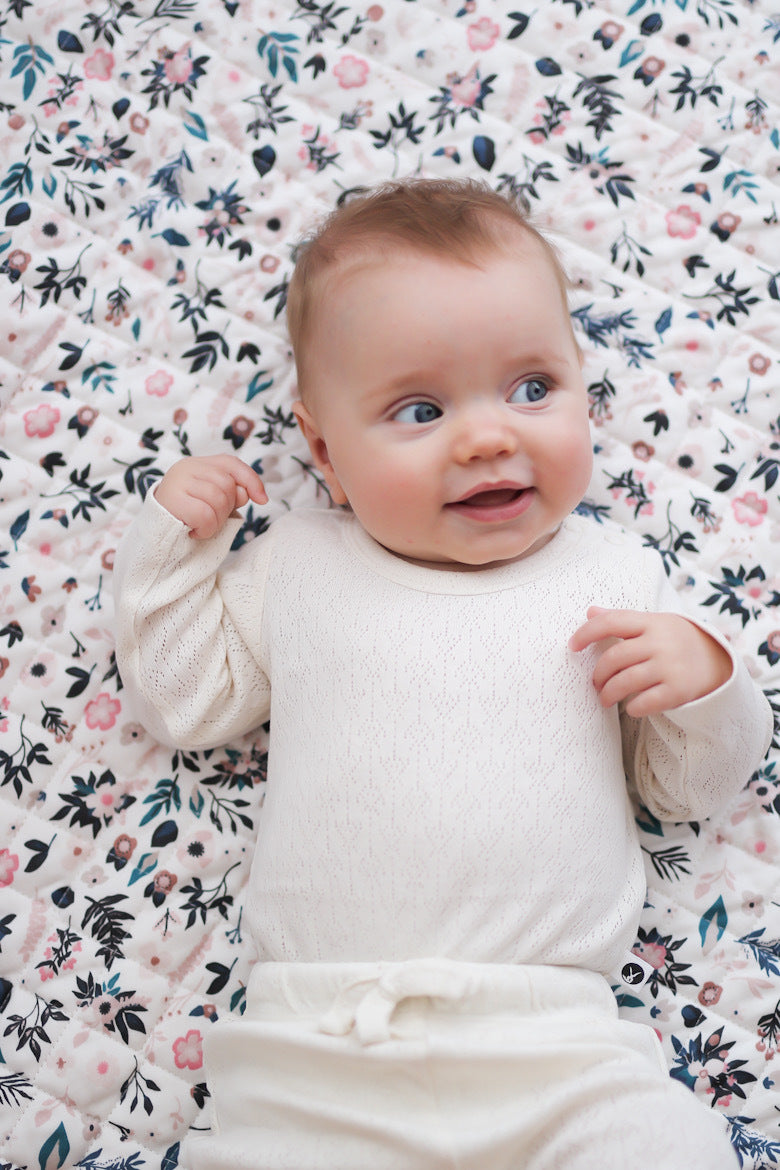 Baby laying on Petite Clementine Quilted Mat while wearing Pointelle Long Sleeve Bodysuit and Baby Pants in Natural, all designed by Brrow and Be