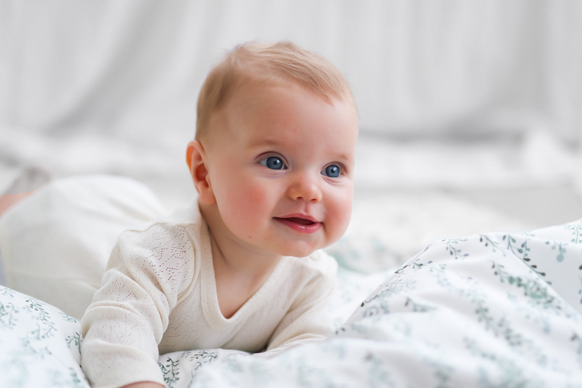 Baby laying on String of Pearls SHeets while wearing Pointelle Long Sleeve Bodysuit and Baby Pants in Natural, all designed by Burrow and Be