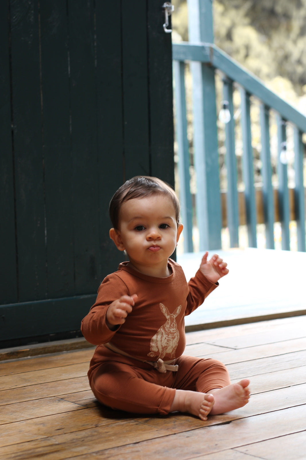 Baby sitting on wooden floor wearing Burrowers Long Sleeve Bodysuit in Chestnut and Marley Pants - Chestnut, designed by Burrow and Be