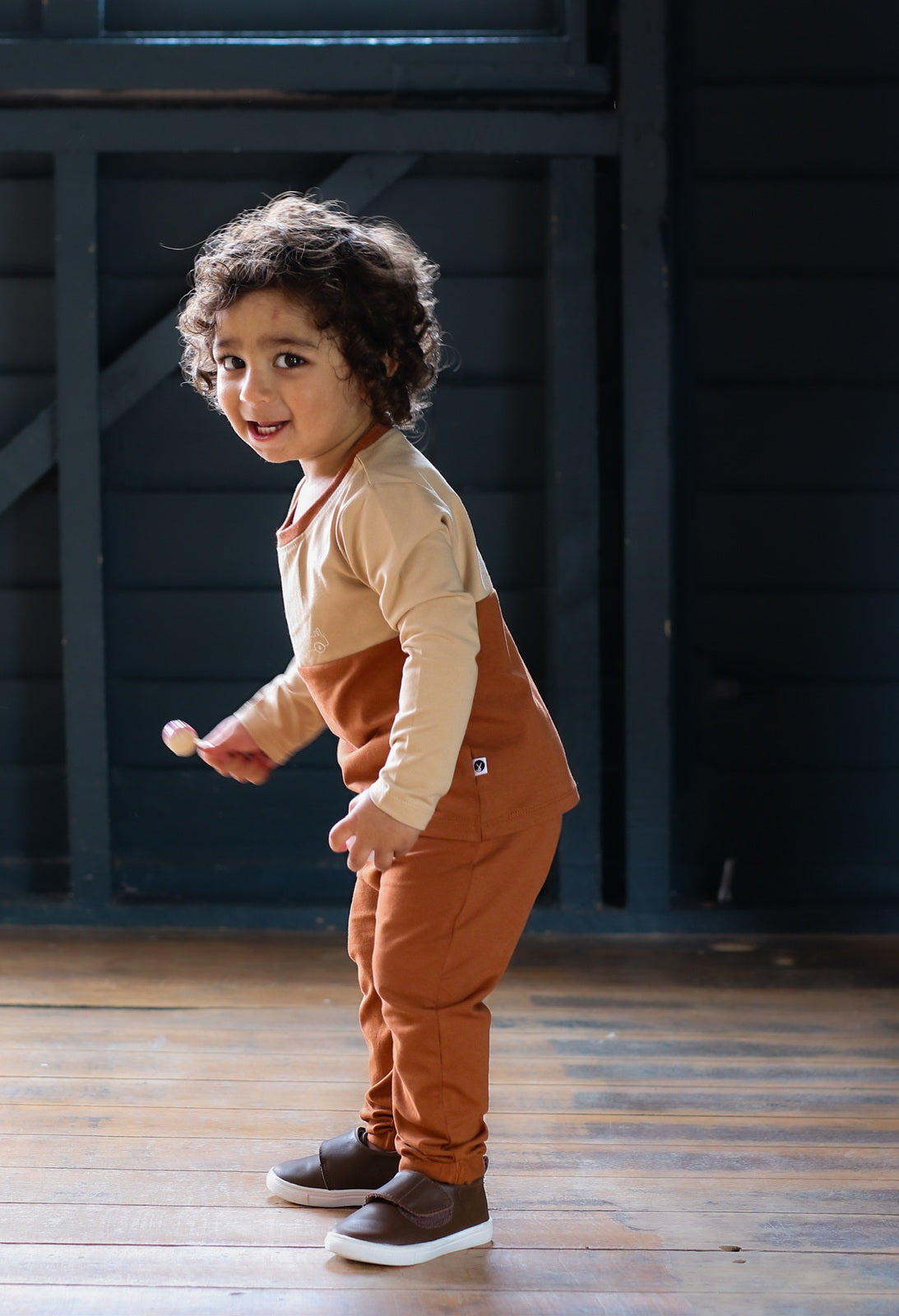 Boy standing on wooden floors, wearing a Long Sleeve T-Shirt, Shoes by Wanders and Marley Pants - Chestnut, all designed by Burrow and Be