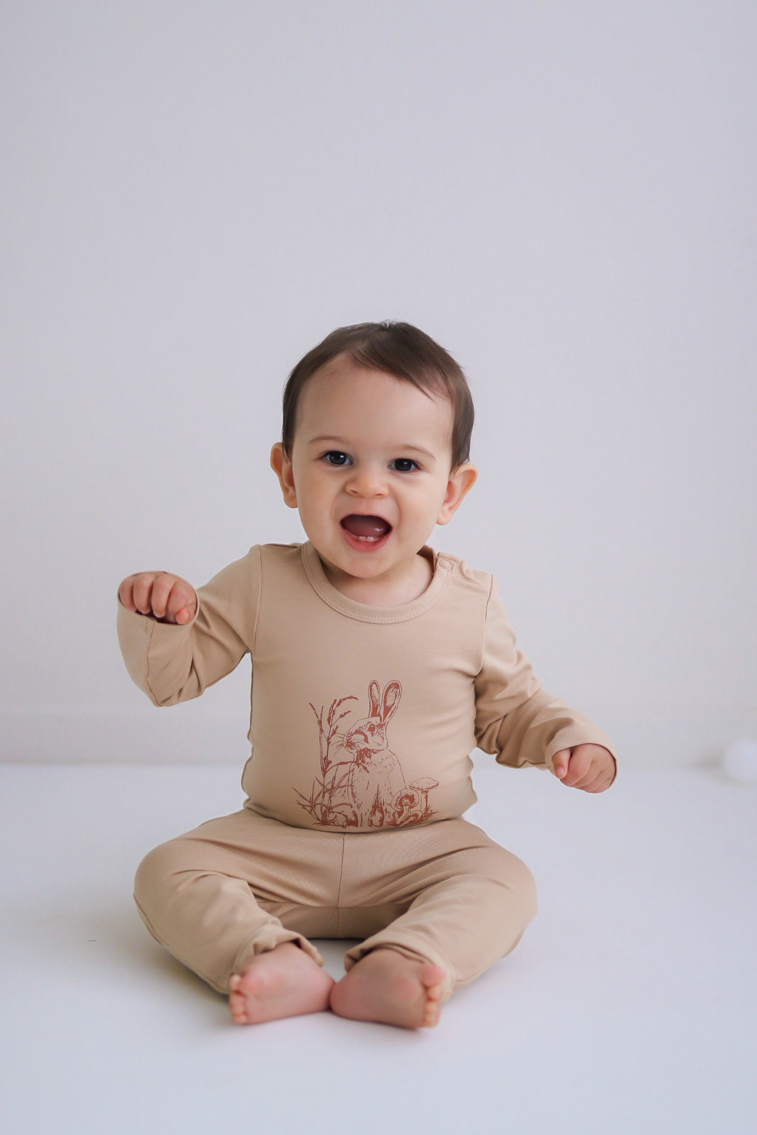 Baby sitting in front of a white background while wearing Burrowers Long Sleeve Bodysuit in Latte and Marley Pants - Latte, designed by Burrow and Be