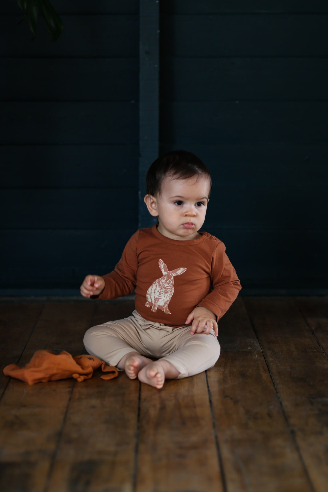 Baby sitting on wooden flooring, wearing Burrowers Long Sleeve Bodysuit in Chestnut and Marley Pants - Latte, designed by Burrow and Be