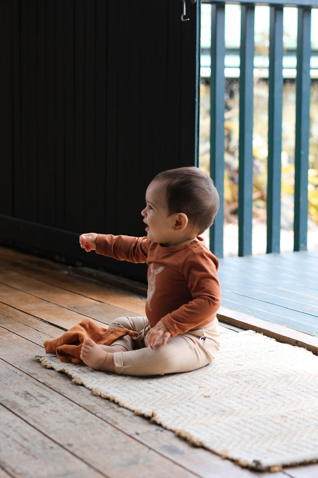 Baby sitting on a carpet laid on wooden flooring, wearing Burrowers Long Sleeve Bodysuit in Chestnut and Marley Pants - Latte, designed by Burrow and Be