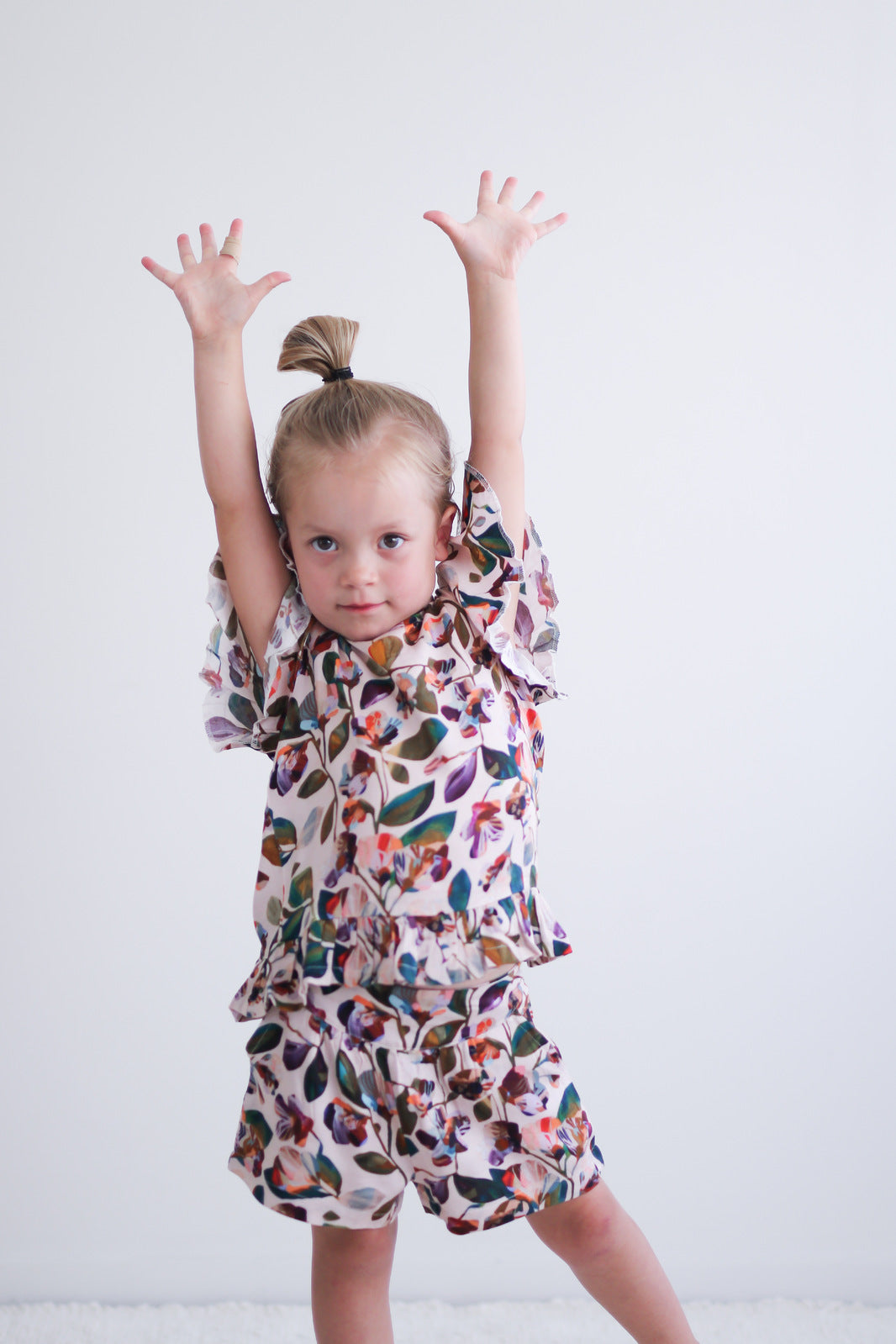 Girl with hand raised wearing Garden Party Ella Top and Garden Party Lyla Shorts by Burrow and Be