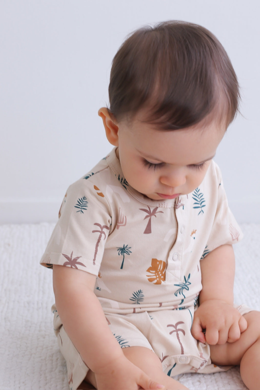Baby sitting and staring while wearing Jungle Stamp Alex Romper from Burrow and Be