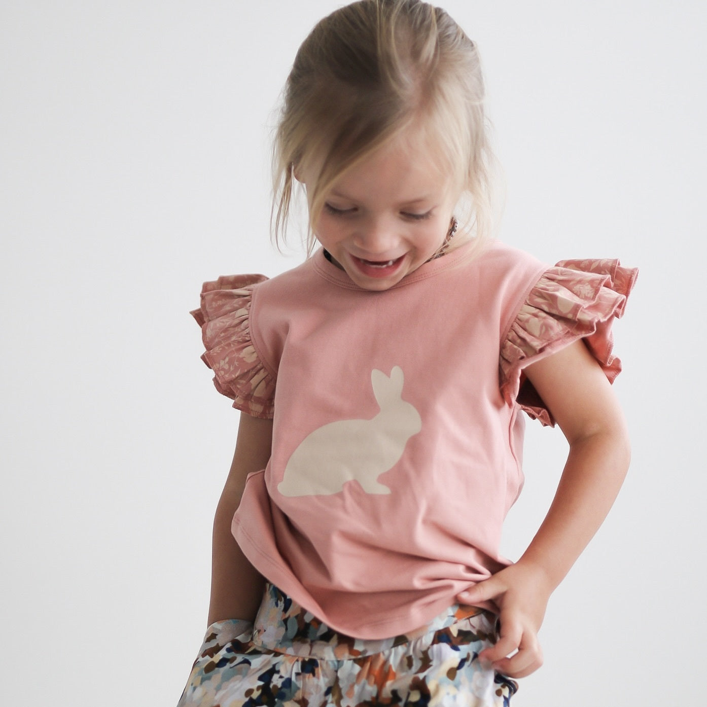 Girl shrugging and wearing Doe Flutter T-shirt and Delight Lyla shorts by Burrow and Be with one hand tucked in the shorts' pockets.