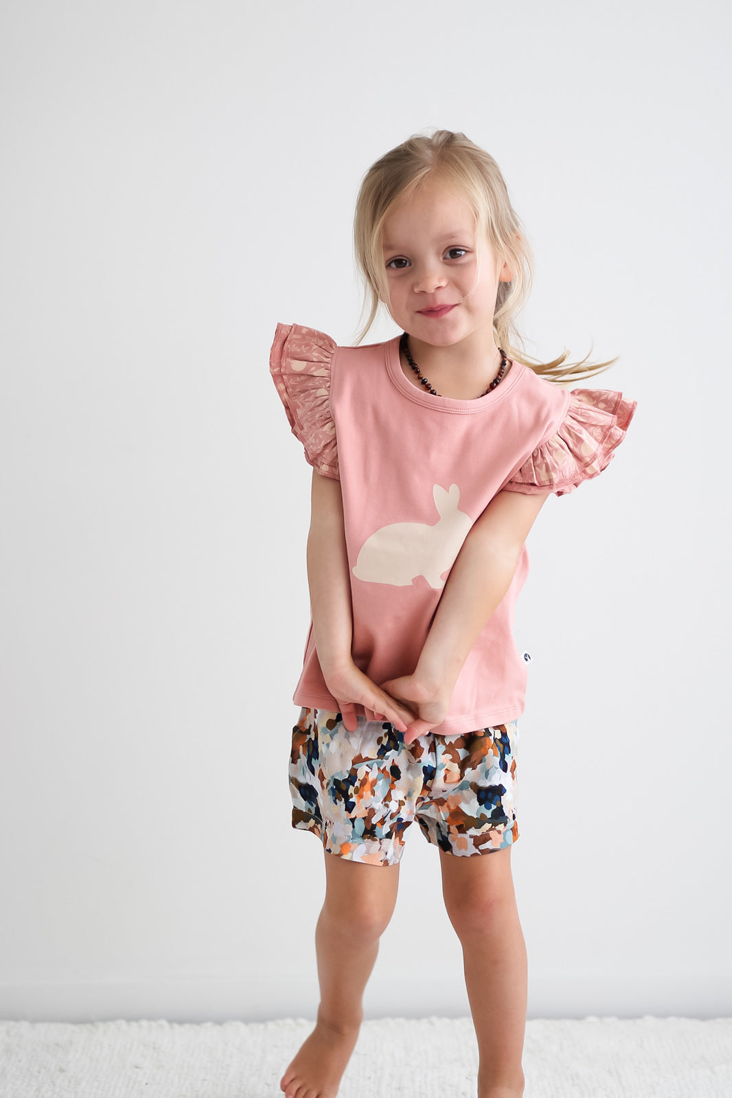 Girl smiling shyly at camera while wearing Doe Flutter T-shirt and Doe Bike shorts by Burrow and Be