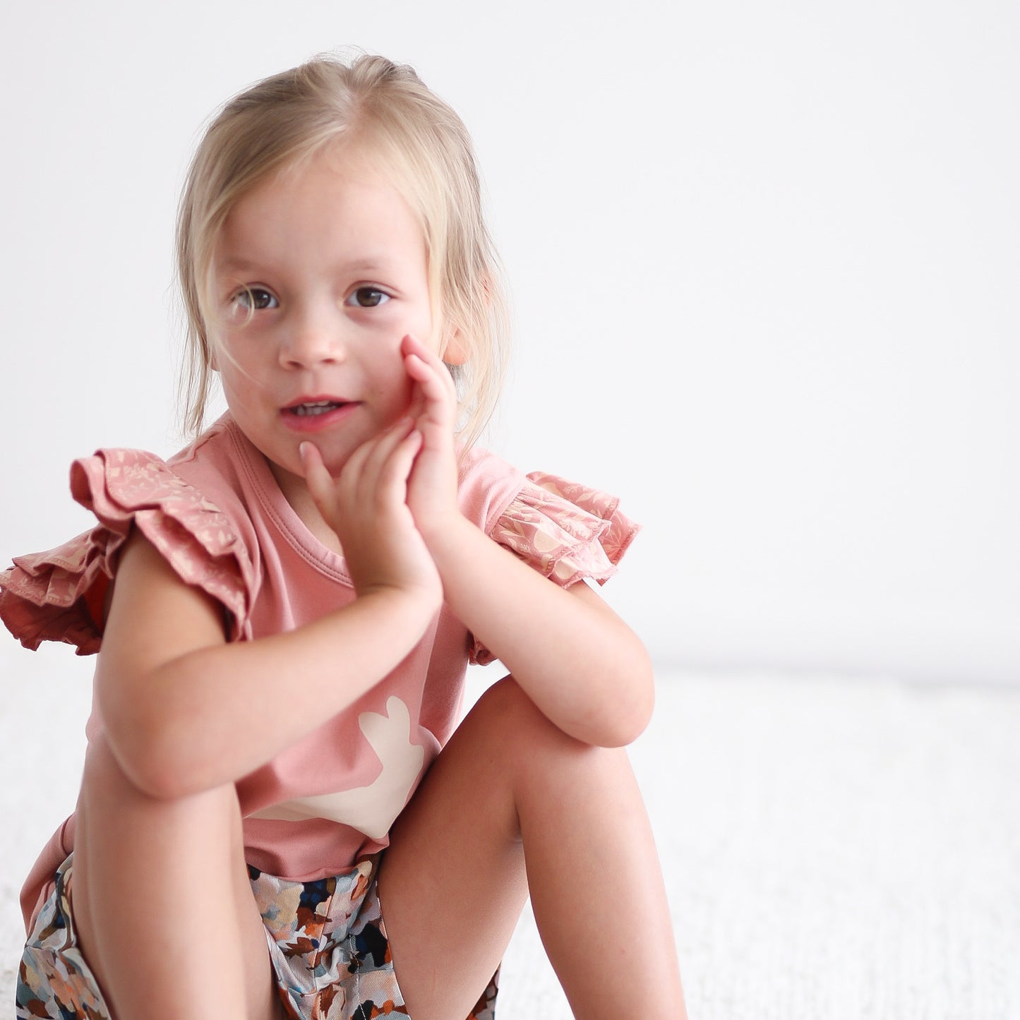 Girl wearing Doe Flutter T-Shirt and Doe Bike Shorts, both by Burrow and Be while sitting and posing in front of the camera against a white background