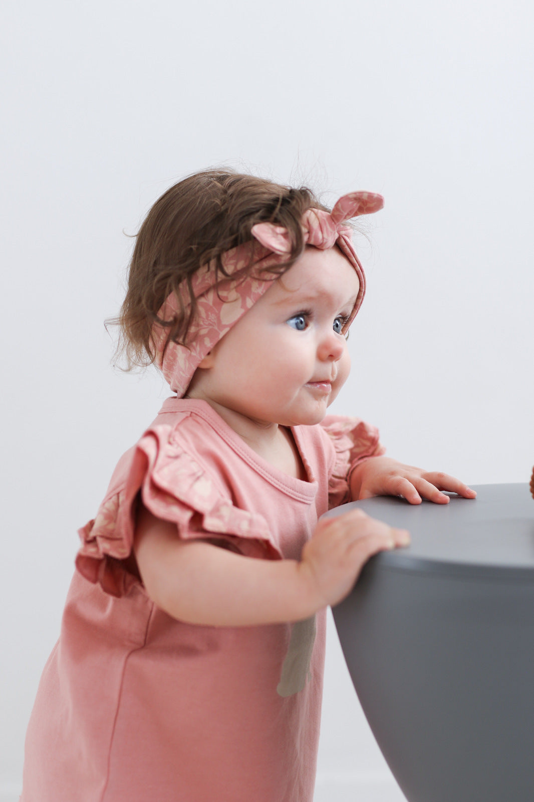 Female baby holding on stool wearing Doe Flutter T-shirt and Mead-Doe headband by Burrow and Be