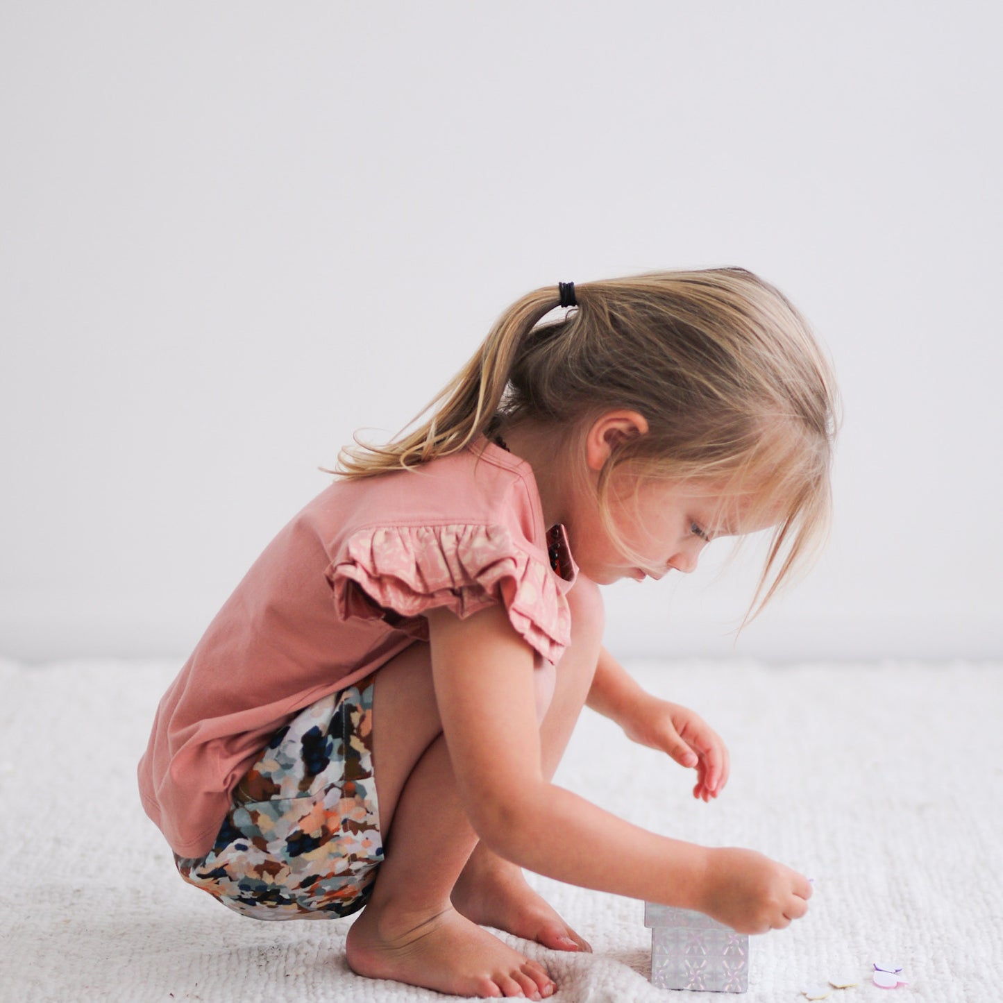 Girl squatting with right side facing camera and wearing Doe Flutter T-shirt and Delight Lyla shorts by Burrow and Be