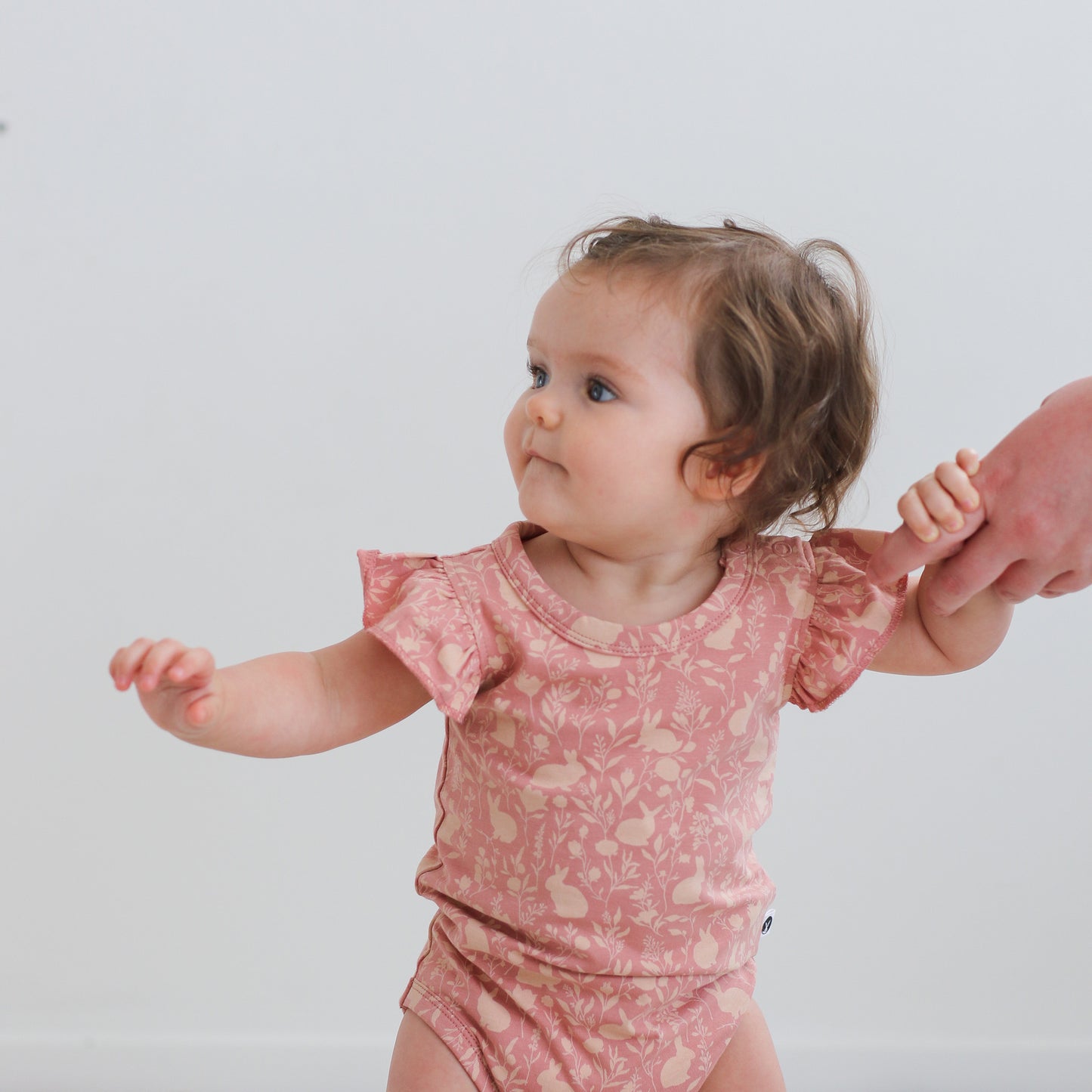 Baby girl standing in front of a white background and posing in Mead-Doe Flutter Bodysuit, designed by Burrow and Be