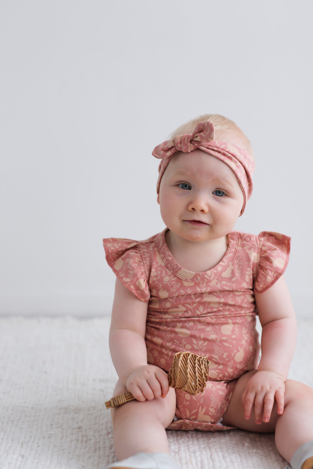 Baby girl sitting on white carpet, wearing Mead-Doe Headband and Flutter Bodysuit, all designed by Burrow and Be