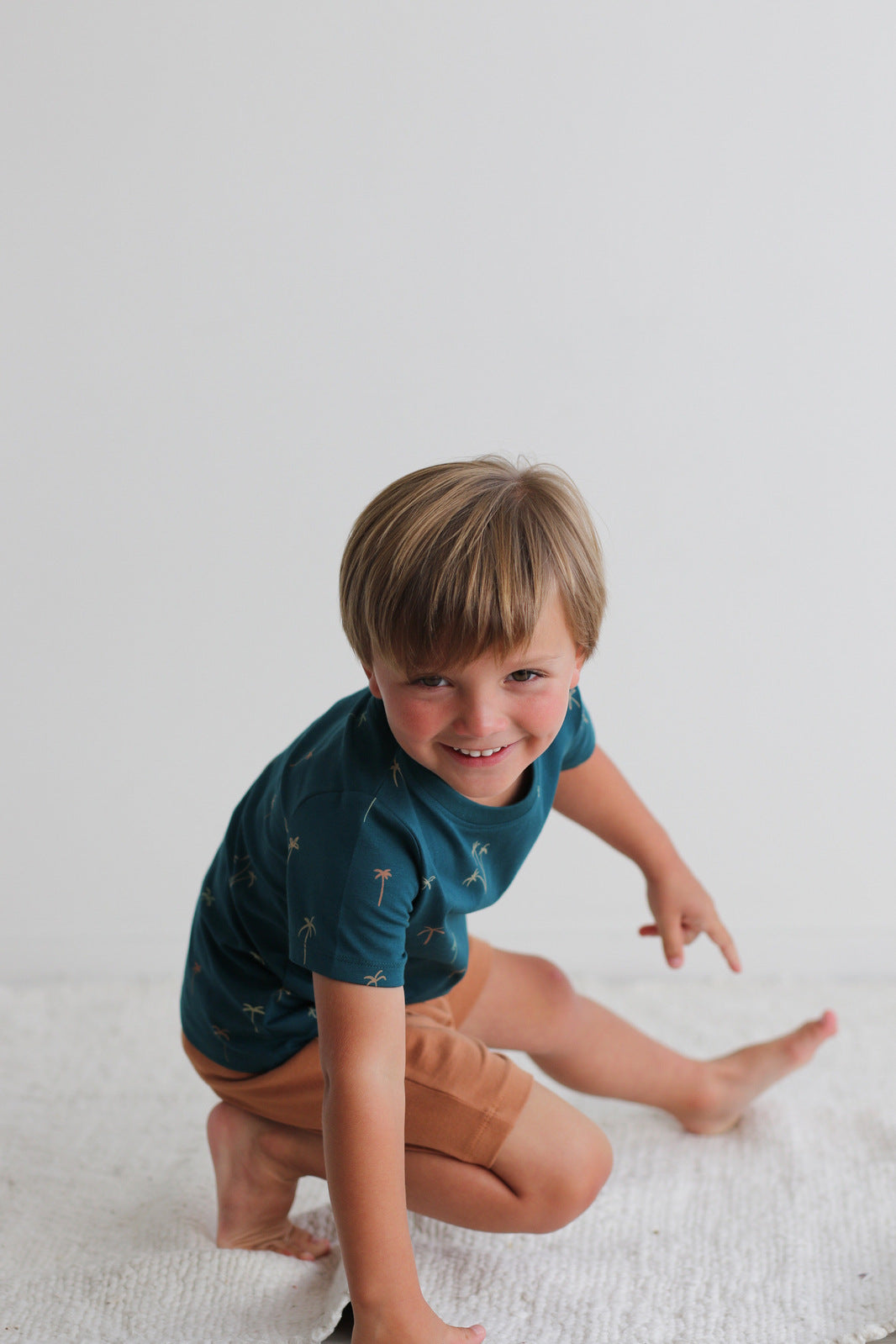 Boy posing against a white background and standing on a white carpet, wearing Palm Classic T-shirt and Leo Shorts in Tan, both designed by Burrow and Be