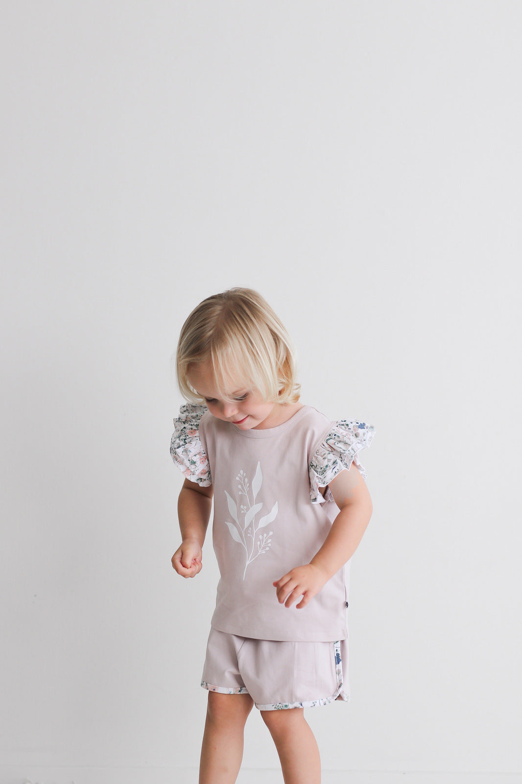 Child looking down while wearing Wildflower/Lavender Penny Shorts and Flutter T-shirt from Burrow and Be