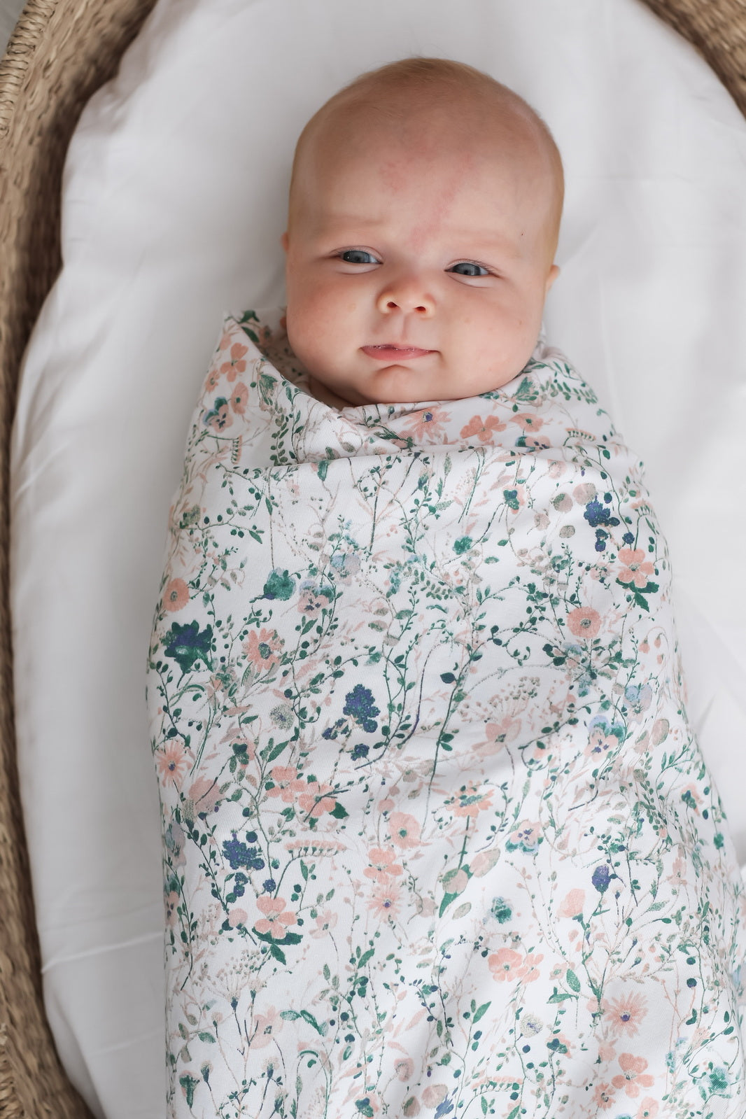 Baby laying in Moses Basket while wrapped in Wildflower Stretchy Swaddle, designed by Burrow and Be